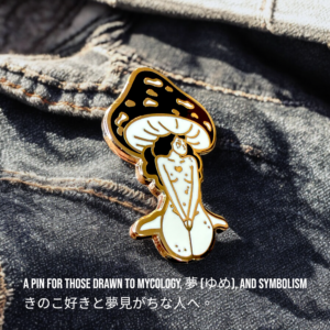 Feminine mushroom figure enamel pin lying on dark textured fabric