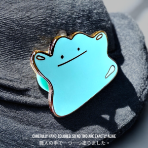 Blue Ditto pin resting on a fabric hat in sunlight