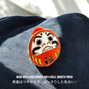 Daruma enamel pin with 福 symbol placed on blue denim