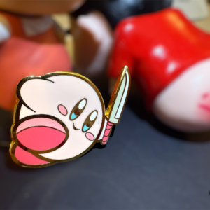 Real-life shot of Kirby enamel pin with toy figure background