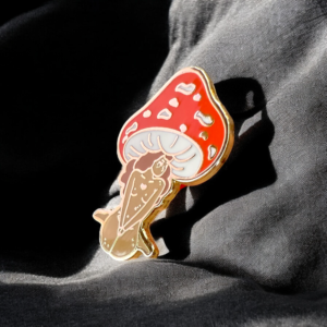 Mushroom enamel pin with feminine figure under red cap on soft shadows