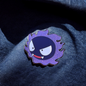 Pokemon enamel pin showing Gastly pinned to denim fabric under natural light