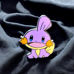 Pokemon enamel pin showing shiny pink Mudkip sitting on soft folds of fabric