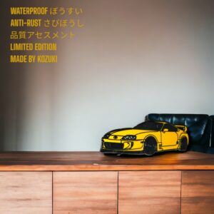 Toyota Supra enamel pin showing yellow Supra MK4 on wooden desk background